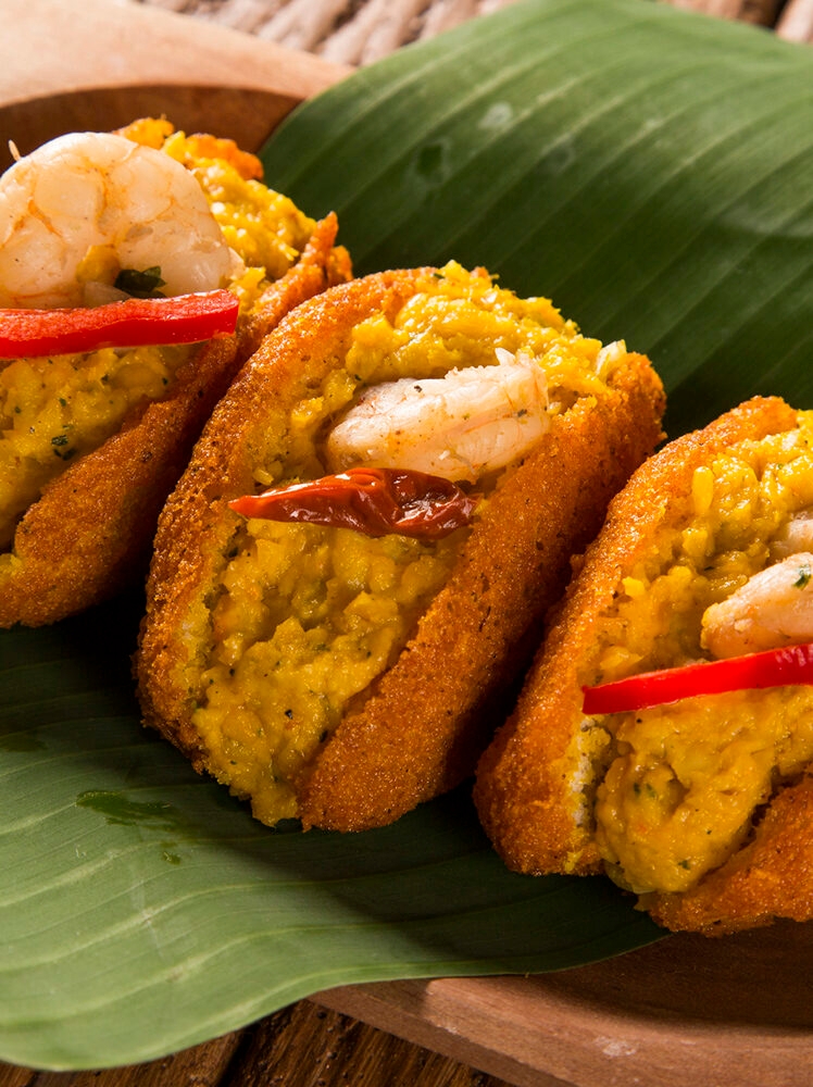 Close-up of three pieces of Acarajé, a Brazilian dish of fried dough filled with shrimp, served on a banana leaf. luxury Brazil holidays.