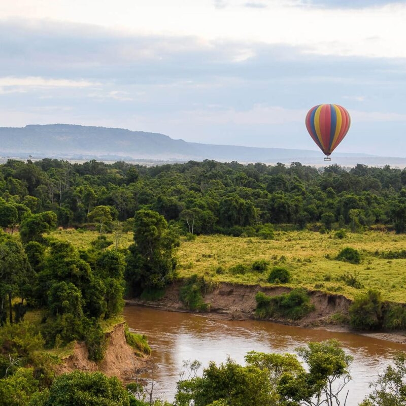 A hot air balloon drifting over a scenic river bend during luxury Maasai Mara holidays.