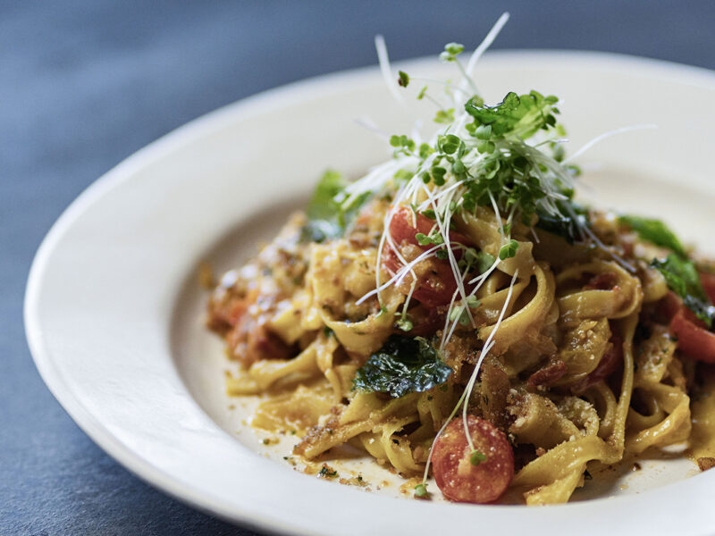 Close-up of fettuccine pasta with tomatoes, basil, and microgreens on a white plate. luxury food and wine holidays.