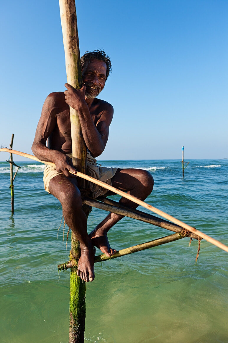 A traditional stilt fisherman perched on a pole in the sea during luxury Indian Subcontinent tours.