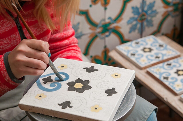 Person painting a decorative ceramic tile for luxury art tours.