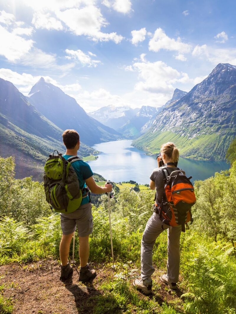 Two hikers viewing a sunlit fjord from a mountain trail during luxury trips for two.
