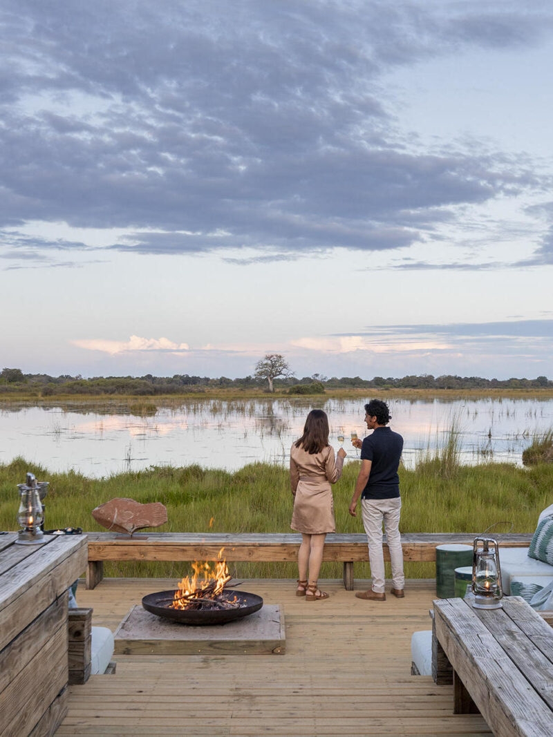 Couple standing on a deck by a fire pit at dusk overlooking a scenic marsh for luxury Honeymoons.
