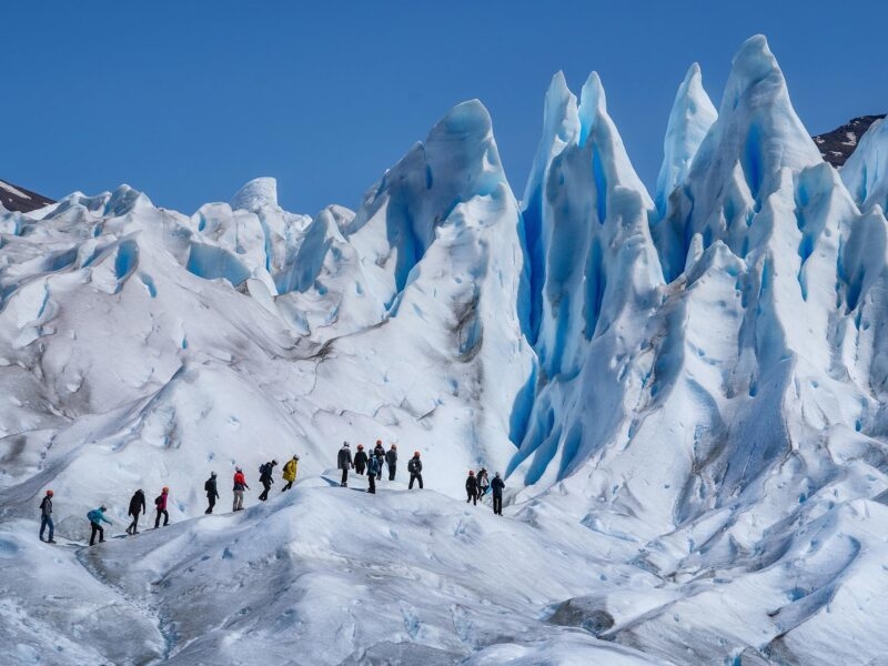 Hikers walk across a jagged blue glacier on one of their epic expeditions.
