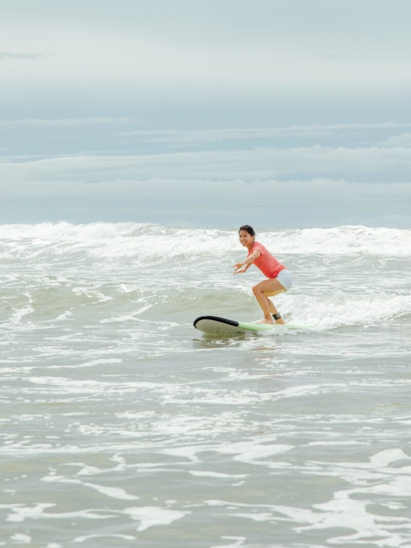 A person in an orange swim suit standing on a surf board on a wave during luxury Latin America family trips.