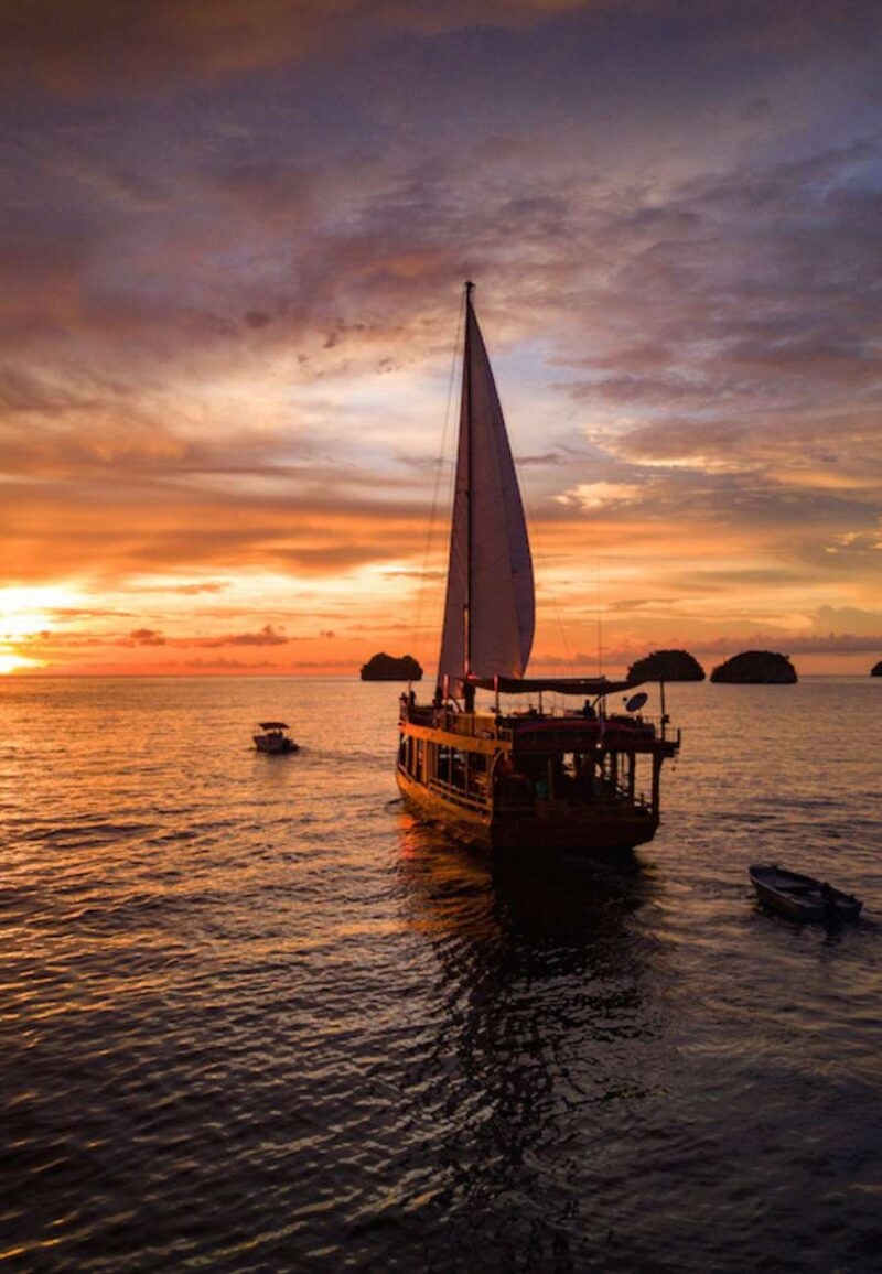 Large sailboat on calm ocean at sunset, part of luxury Southeast Asia tours.