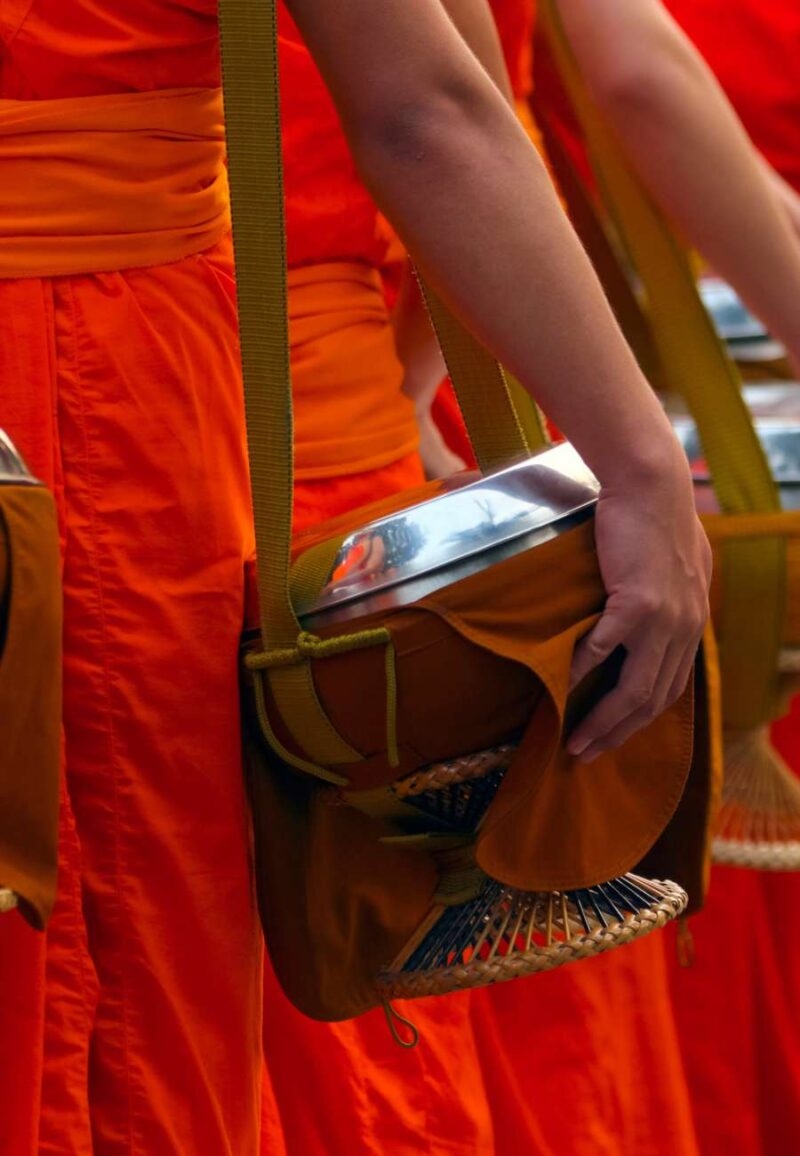 Buddhist monks in orange robes holding alms bowls during luxury Southeast Asia tours.