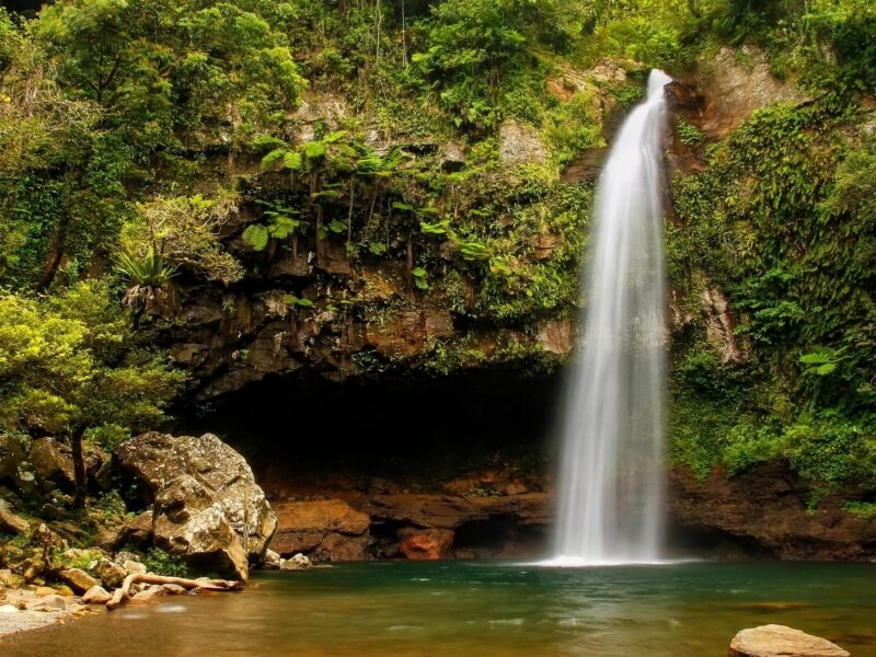 A white waterfall flowing down a rocky cliff into a pool surrounded by lush rainforest for luxury Fiji vacations.