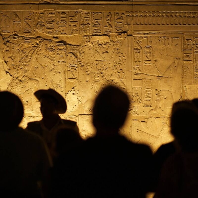 Luxury Egypt Tours - silhouettes of people looking at ancient hieroglyphs on a lit wall