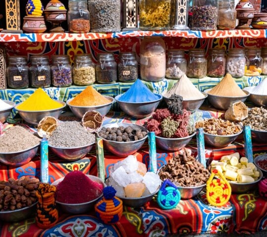Bowls of colourful powdered spices and whole spices on a brightly patterned table cloth