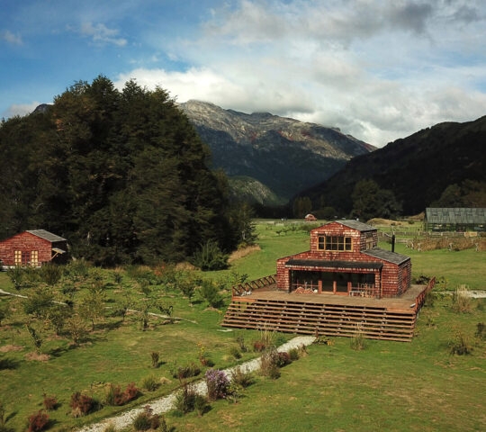 A lush valley with a clear blue river, surrounded by forests and mountains under a cloudy sky.