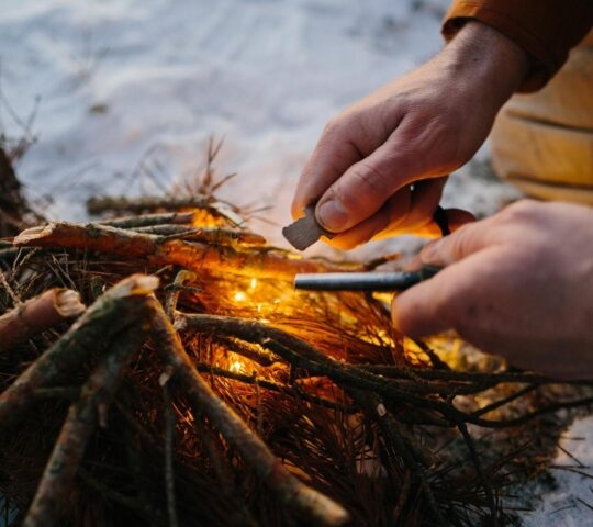 Closeup of male hand starts fire with magnesium fire steel, fire striker. Survival concept