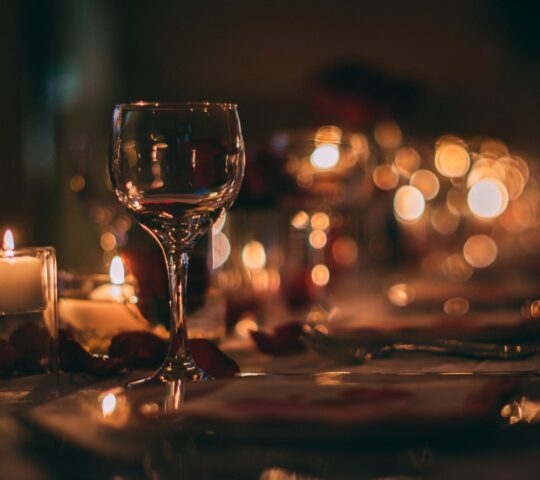 Elegant dinner setting with a wine glass, candles, and warm bokeh lights.