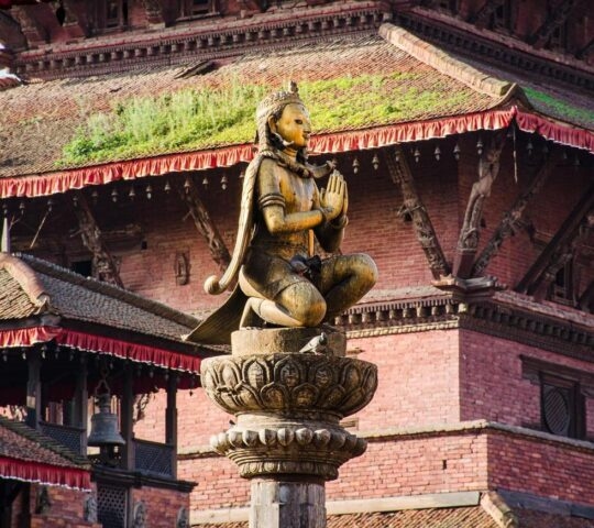 Statue of Malla King on top af o column, amongst Patan Durbar square temples in Kathmandu, Nepal