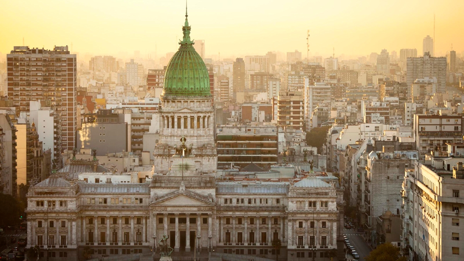 Sunset view of a grand domed building amidst a densely packed cityscape.