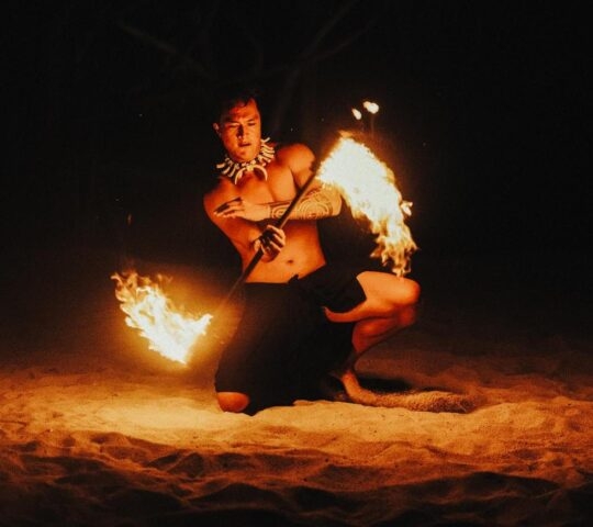 Person performing fire dance on sandy beach at night.