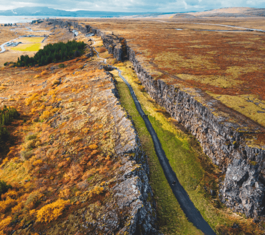 Aerial view of a road bisecting rocky cliffs with autumn-colored foliage on either side.