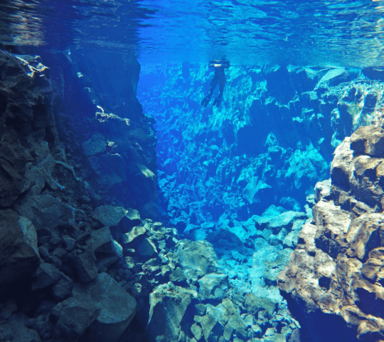 Underwater view of a silhouetted diver exploring the clear waters between rocky formations.