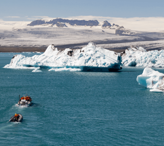 Tour boats navigate among icebergs in a glacial lagoon with a snowy mountain backdrop.