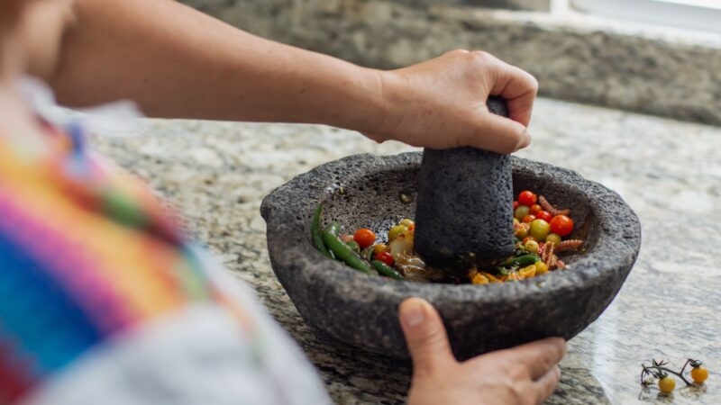 Person grinding spices in a stone mortar and pestle.