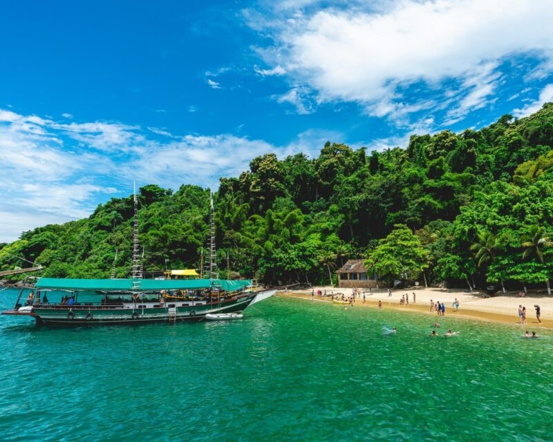 A boat moored in the shallow green water next to a beach near Paraty, Brazil