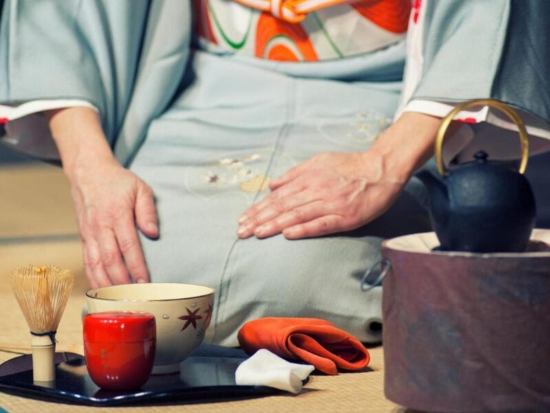 Scene from Japanese tea ceremony with a geisha kneeling on the floor next to cups