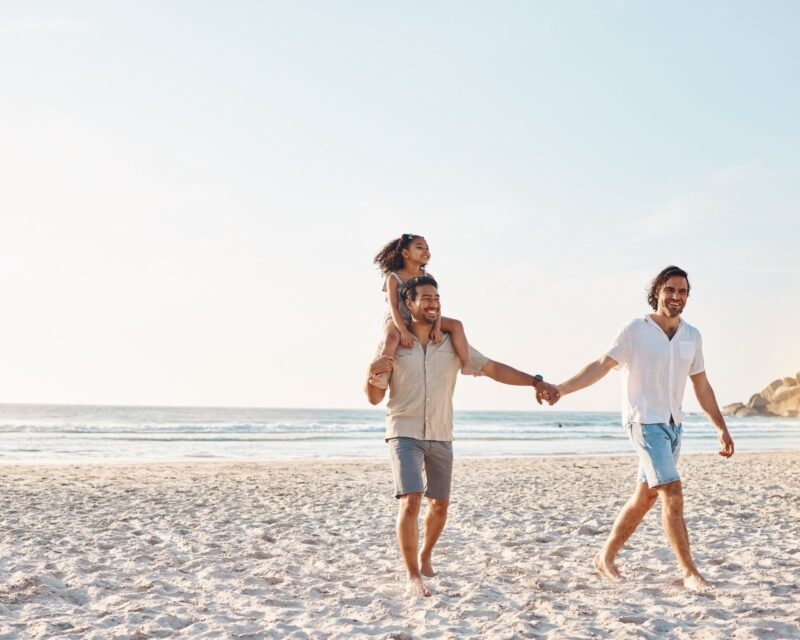 A gay couple walking on the beach with a small child