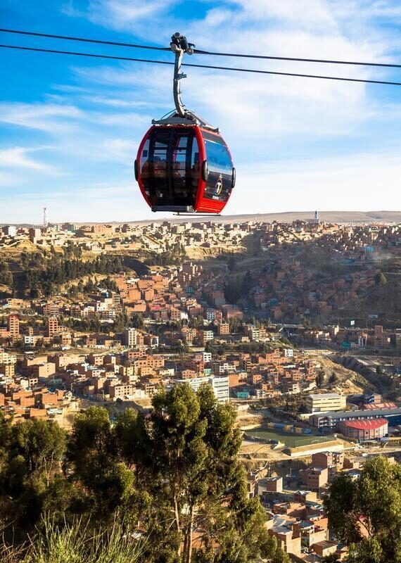 View of La Paz Bolivia and the peak of Huayna Potosi mountain in the background with a red teleferico cable car public transportation system and many houses in the distance with beautiful blue skies