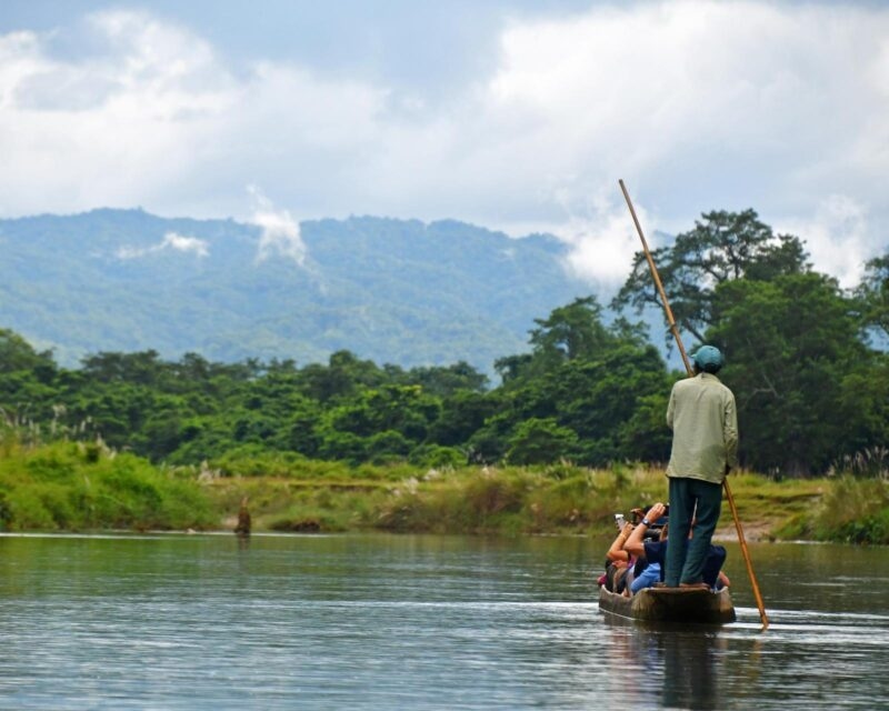 River trip in the Nepalese Jungle Chitwan National Park Nepal showing a man guiding a canoe in a family trip