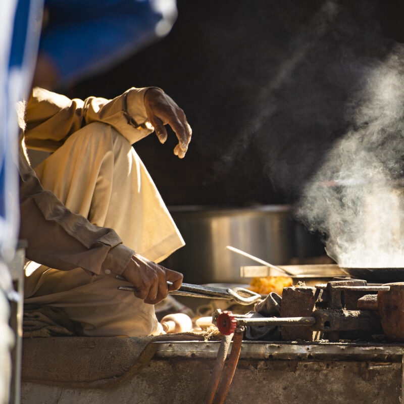 An Indian elderly man is cooking Chapati on the streets of Nepal