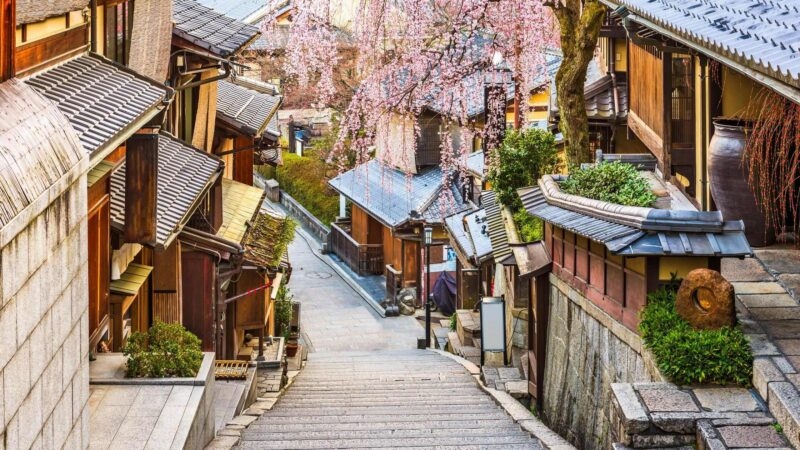 Stone staircase street lined with traditional wooden buildings and blooming pink cherry blossoms.