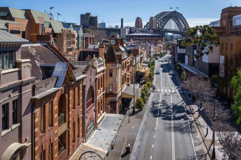 Elevated view of historic brick buildings along a street with the Sydney Harbour Bridge visible in the distance.