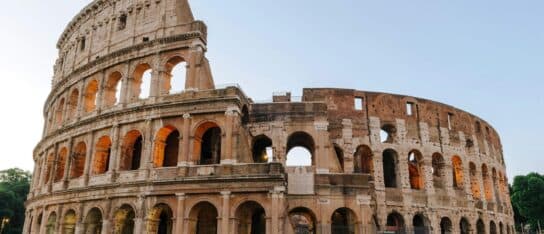 The ancient stone exterior and arched levels of the Colosseum under a bright sky.