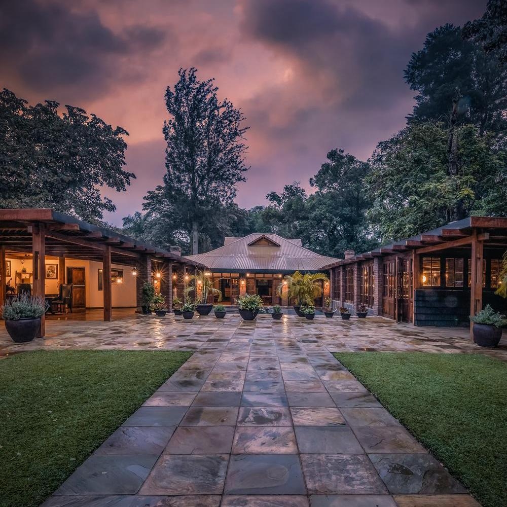 Stone path leading to the Arusha Coffee Lodge reception under a purple sunset sky with potted plants and trees.