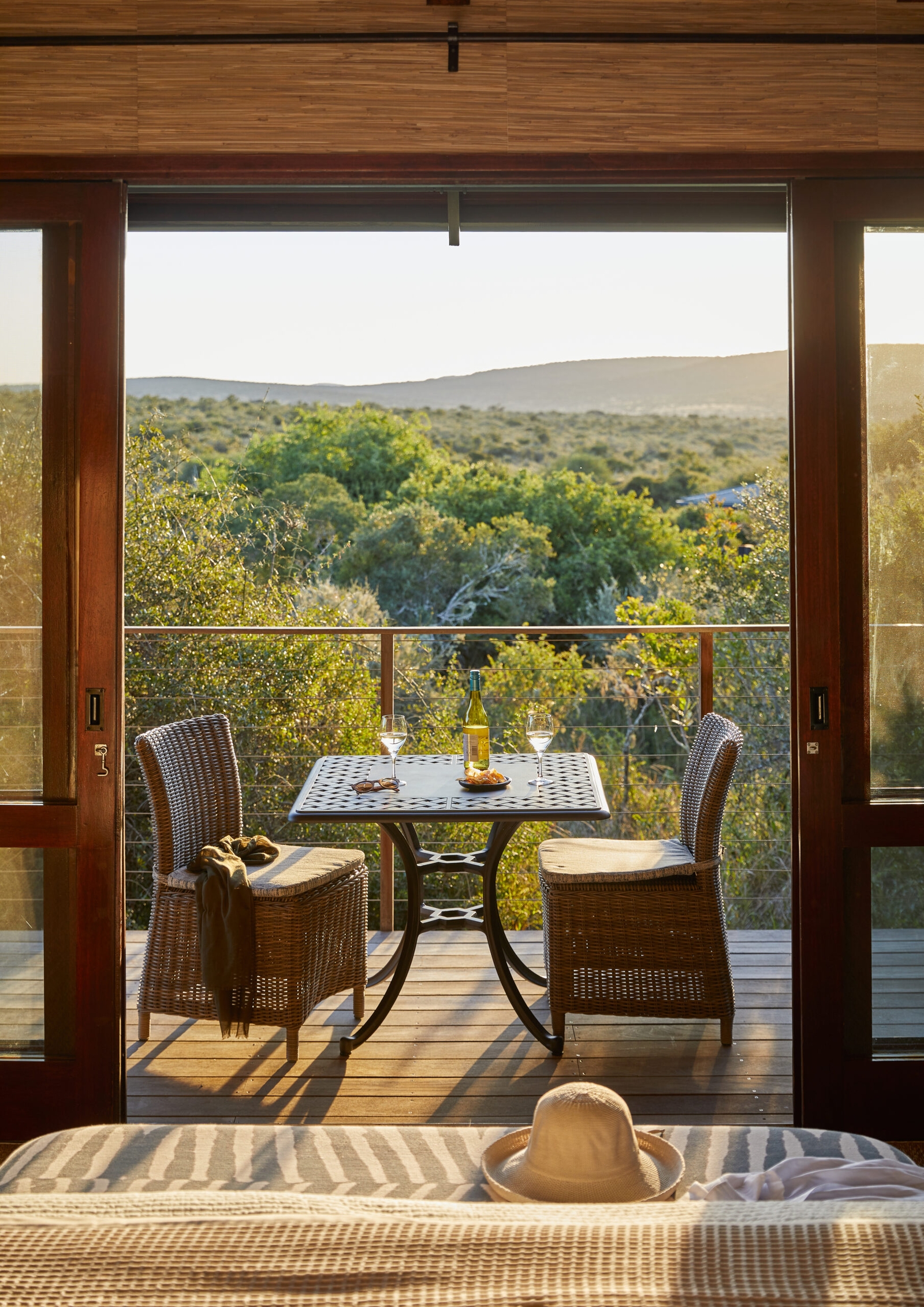 Balcony with table set for two overlooking a lush forest at sunset.