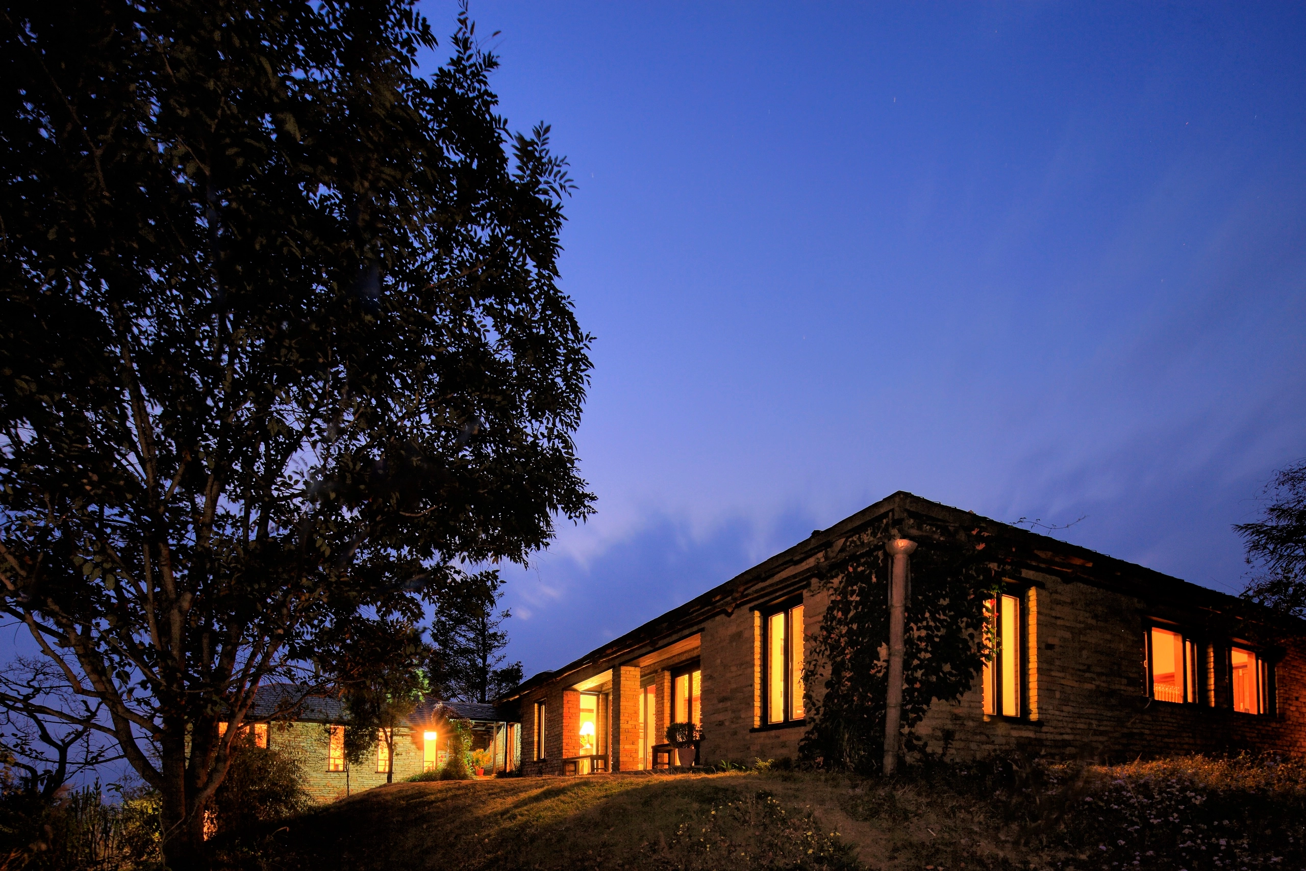 Illuminated brick house at dusk with a blue sky and wispy clouds.
