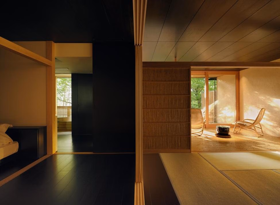 Minimalist Japanese suite with dark floors, tatami mats, and a bright terrace overlooking a garden.