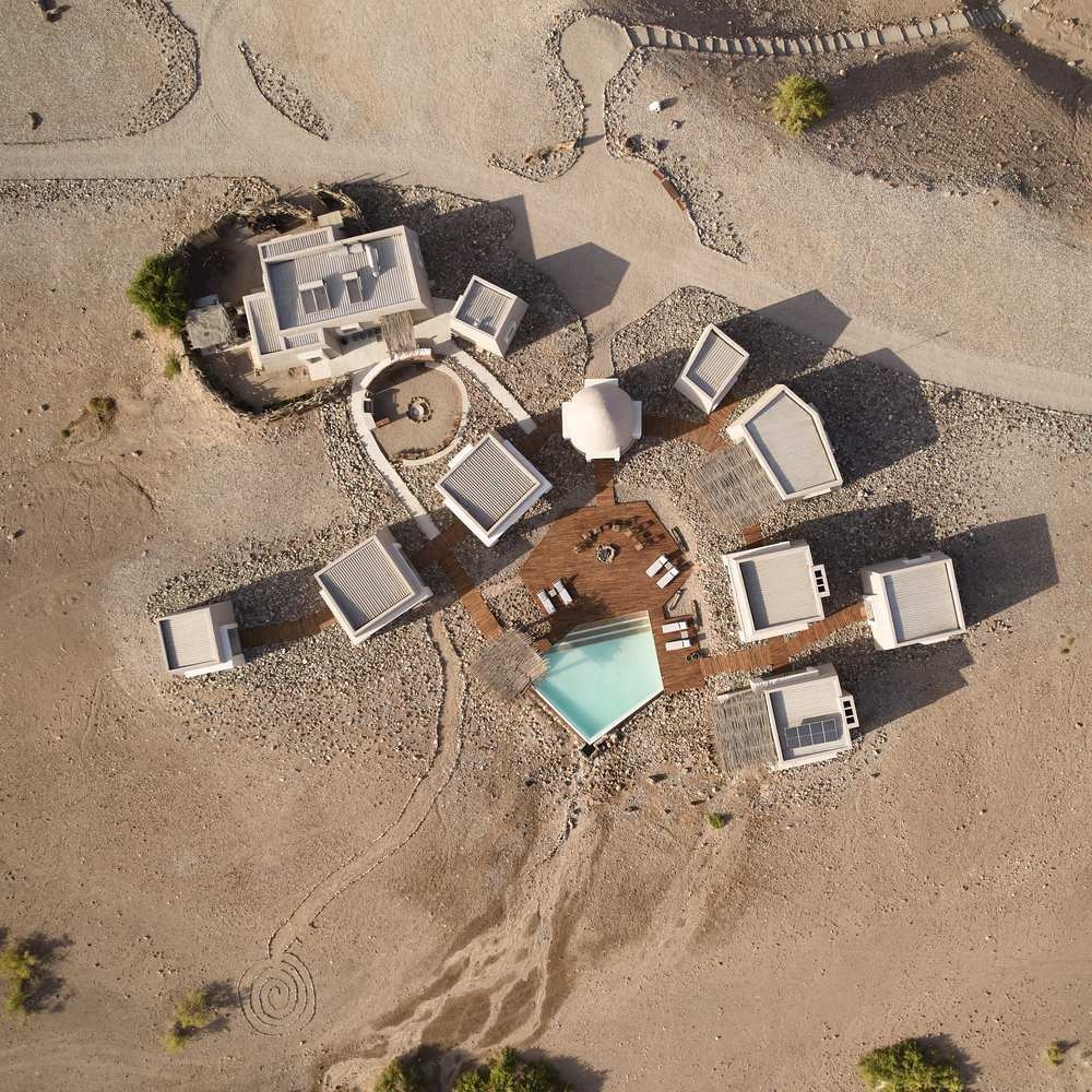 Aerial view of a modern desert lodge with white buildings, a central pool, and wooden decks in a desert landscape.