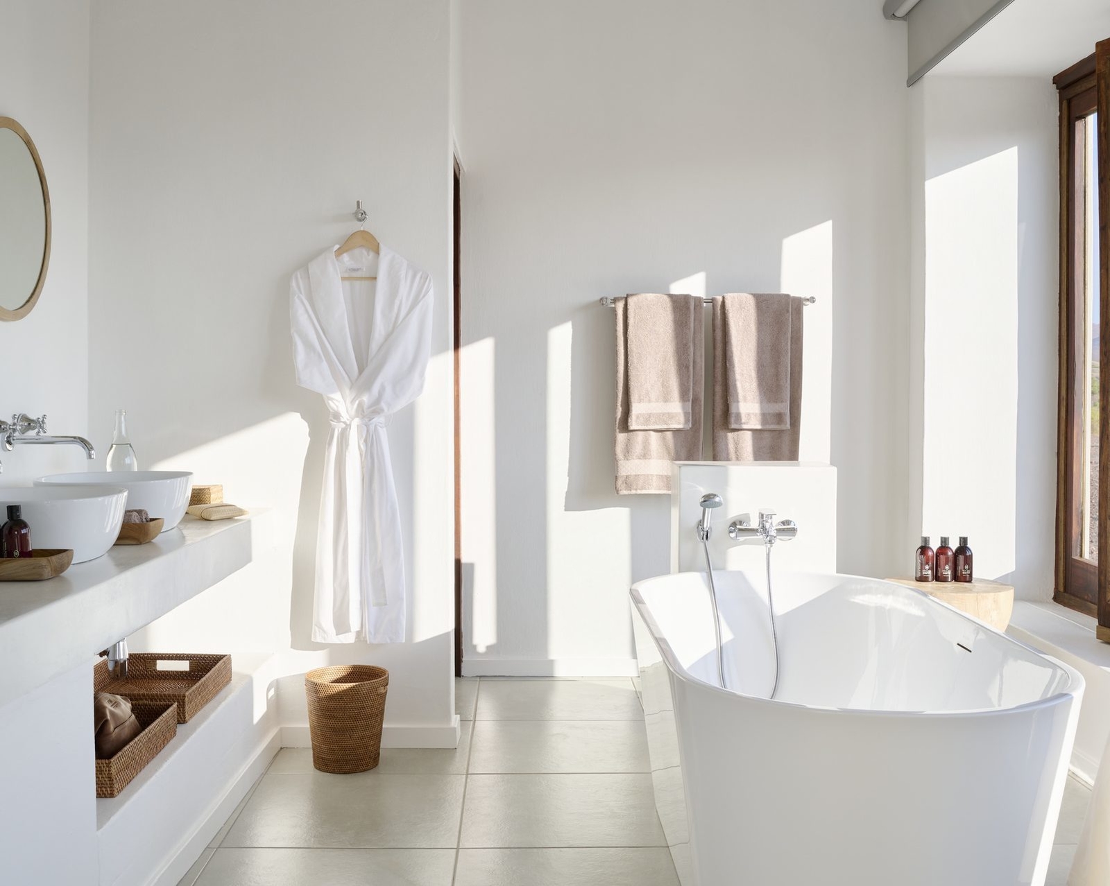 Modern white bathroom with a freestanding tub, double vanity, and a white bathrobe hanging on the wall.