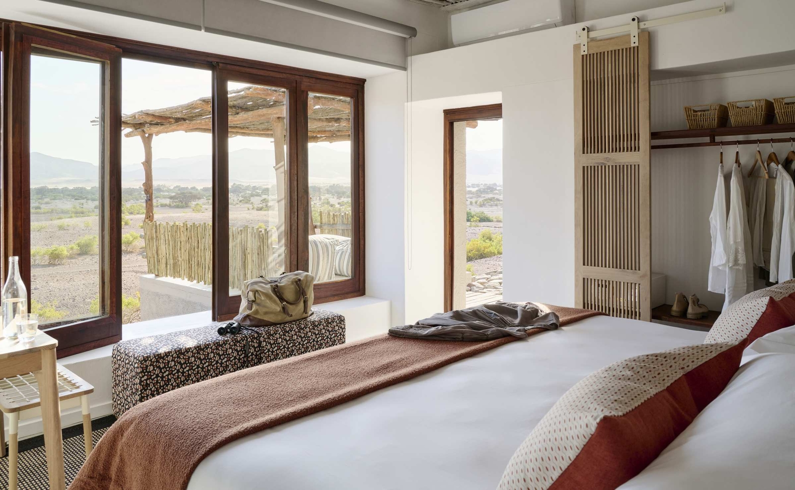 Bedroom with a king bed, open closet, and large glass doors leading out to a desert deck.
