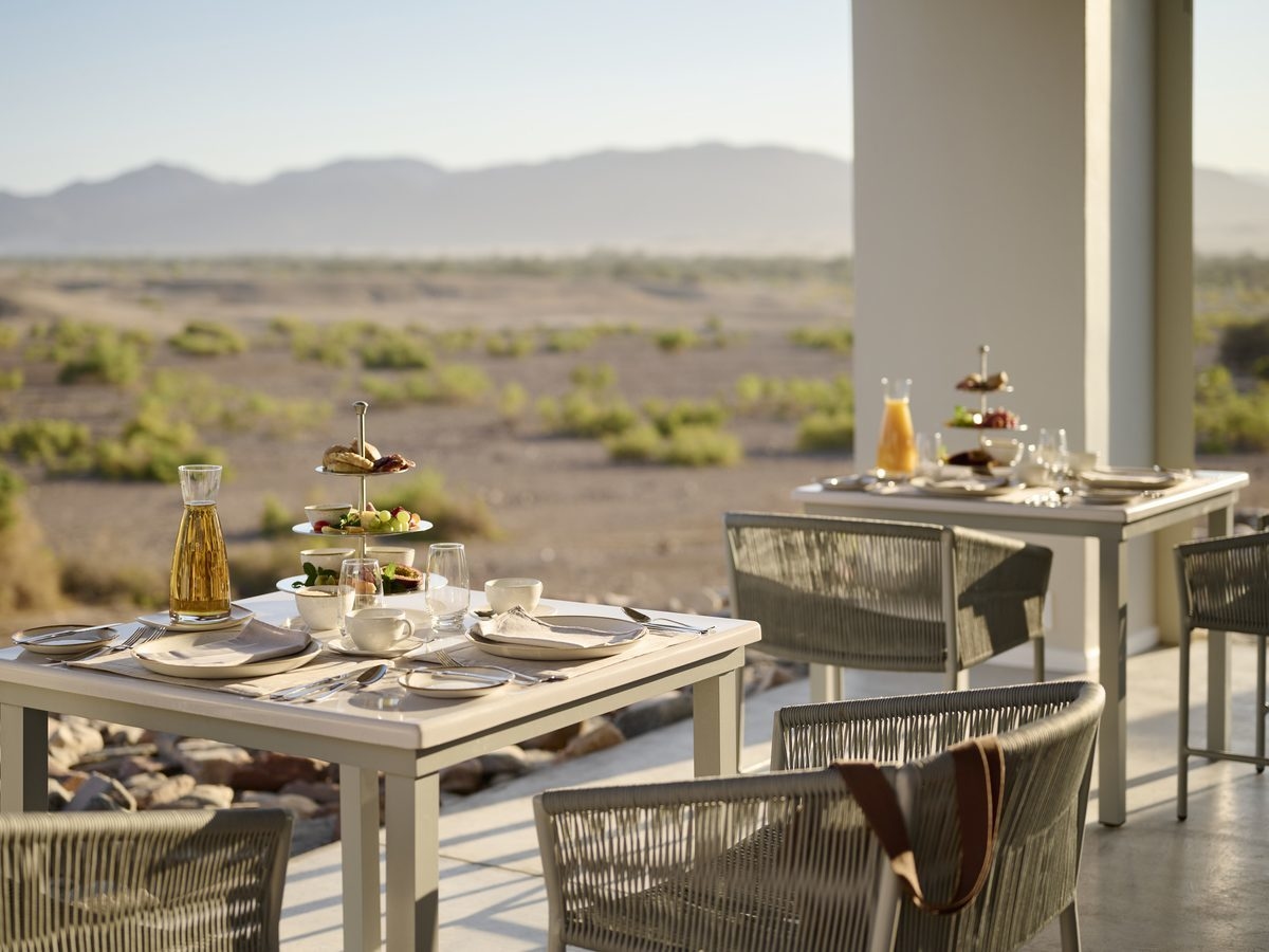 Breakfast tables set on a patio overlooking an expansive desert landscape.