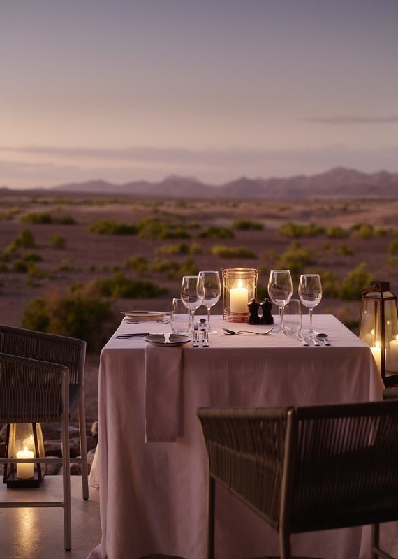 Candlelit table for two set for dinner on a patio overlooking a vast desert landscape at dusk.