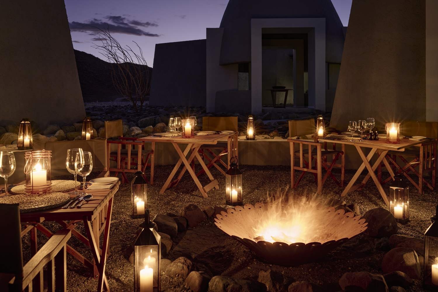 Candlelit outdoor dining area around a blazing fire pit at twilight.