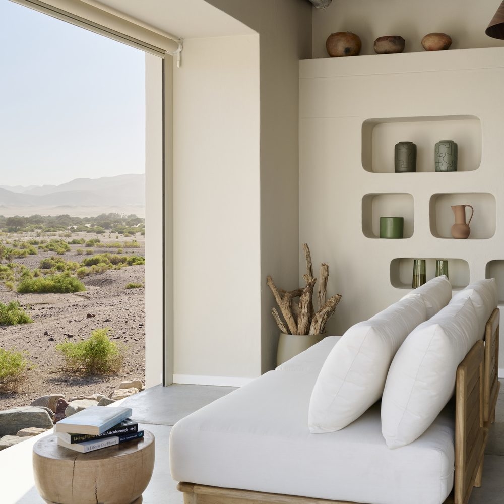 Minimalist room with a white sofa looking out at an open desert landscape, with David Attenborough books on a side table.