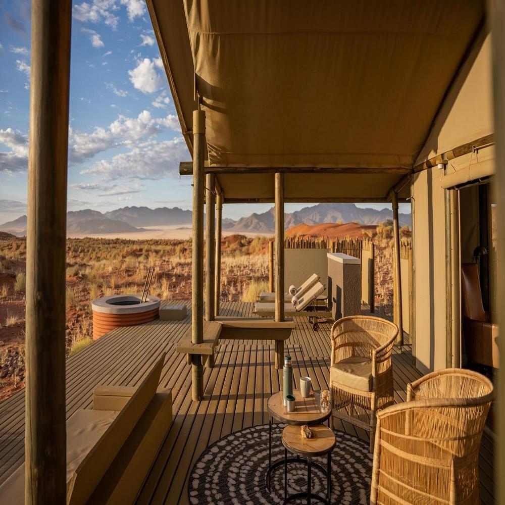 Elevated wooden deck with wicker chairs and a small table looking out over red sand dunes.