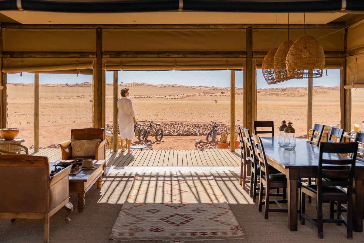 : Open-air lodge interior with a dining table and lounge chairs looking out over the desert.