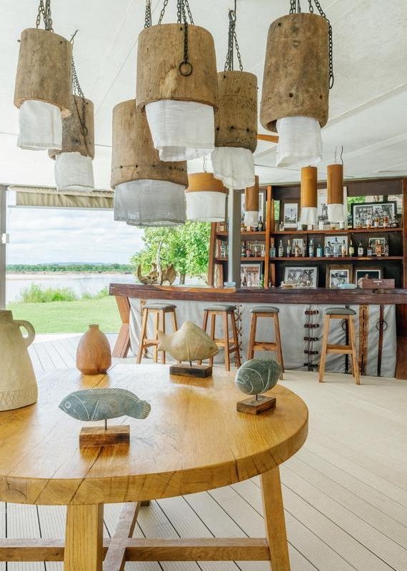 Open-air bar with wooden stools, hanging rustic lights, and a foreground table displaying two stone fish sculptures.