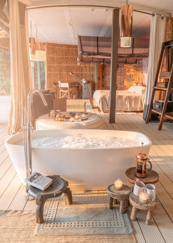 Luxury tent interior featuring a freestanding bathtub, candles, and a stool holding a book titled Wild Signs Star Paths.