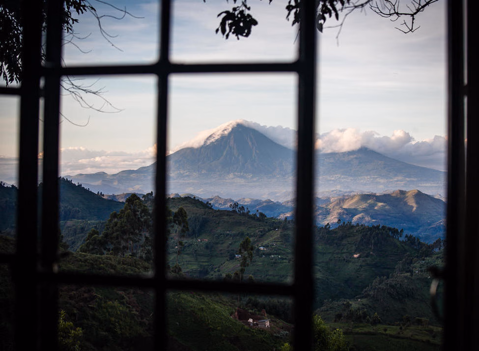 View through a window of a towering volcano and lush green hills at Clouds Lodge Uganda.