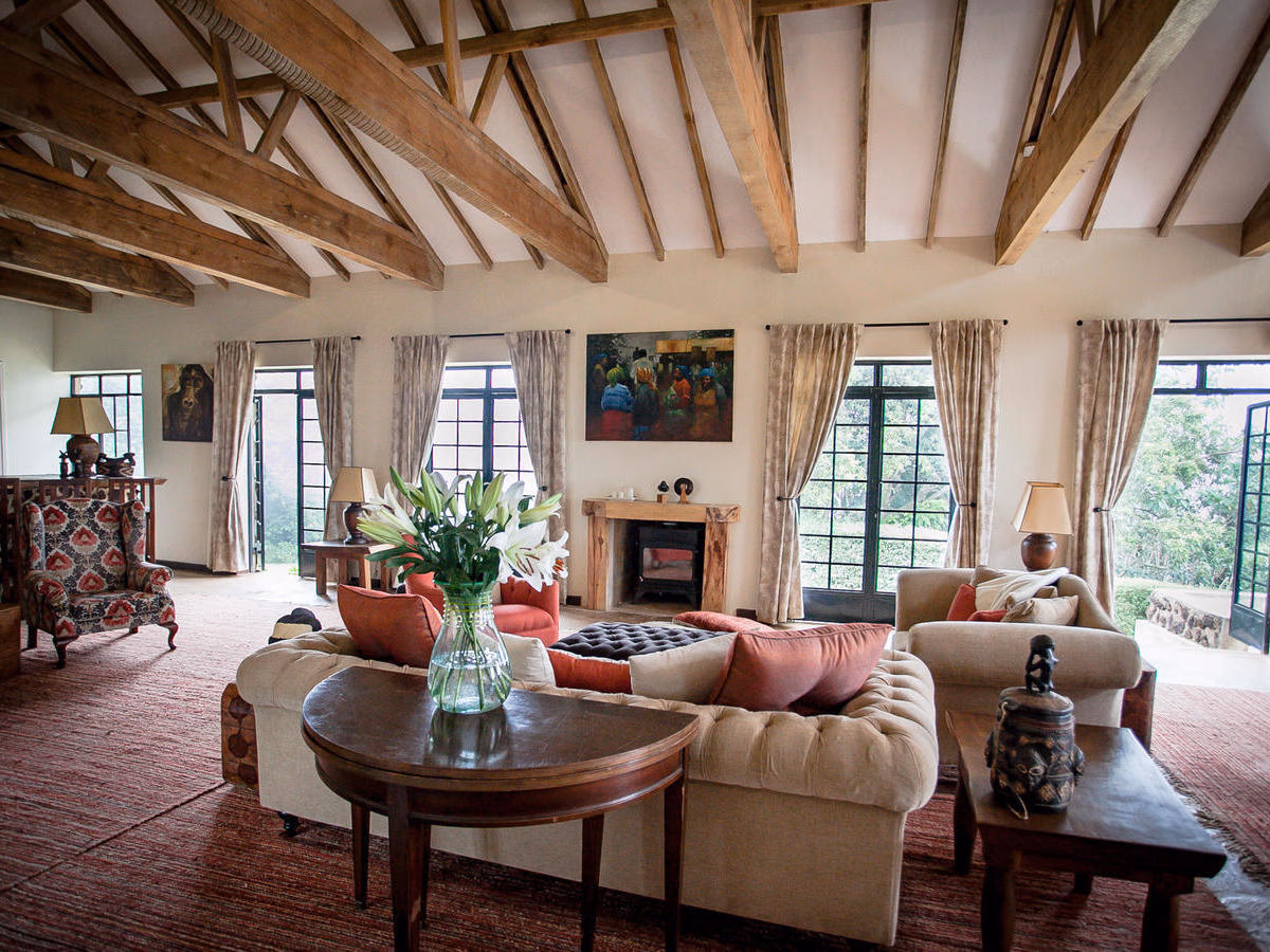Spacious sitting room at Clouds Lodge Uganda with wooden beams, sofas, fireplace, and white lilies.